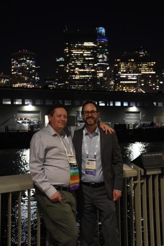 Two people standing in front of the SF skyline at night